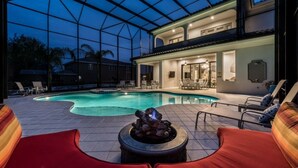 Un área junto a la piscina con una chimenea, sillones de descanso y un porche cubierto.
