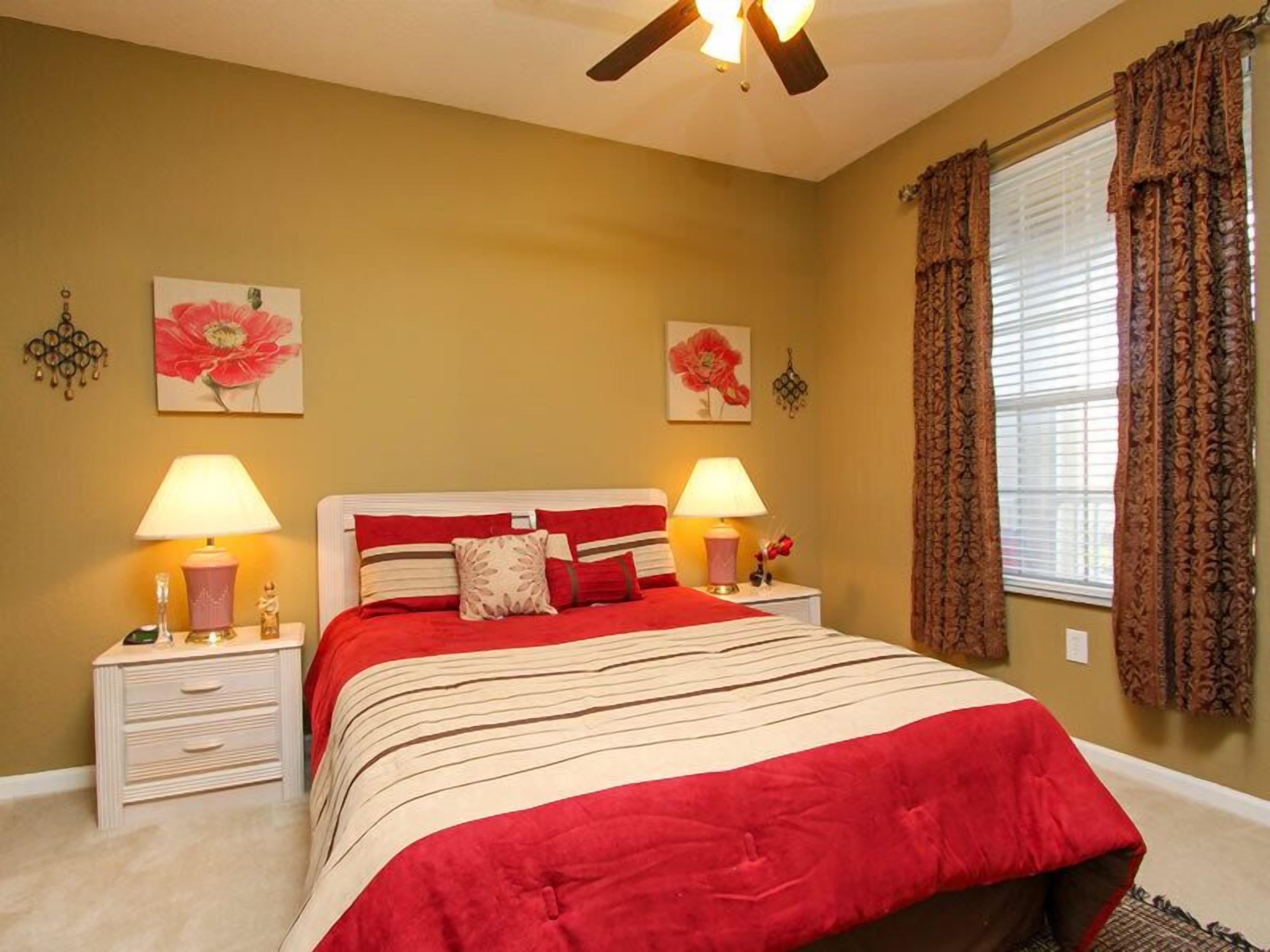 A bedroom with a bed, two bedside tables, a ceiling fan, and two wall-mounted lamps.