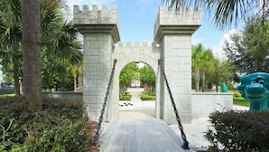 A stone archway leading to a pathway, surrounded by greenery and a large blue statue.