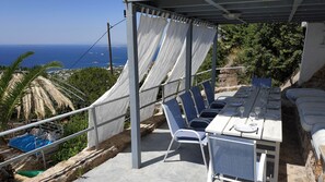 A terrace with a table set for dining, overlooking a coastal view. - Infinity Blue Suites (Saronikos)