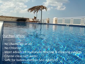 A clear pool with a tropical umbrella and lounge chairs. - Infinity Blue Suites (Saronikos)