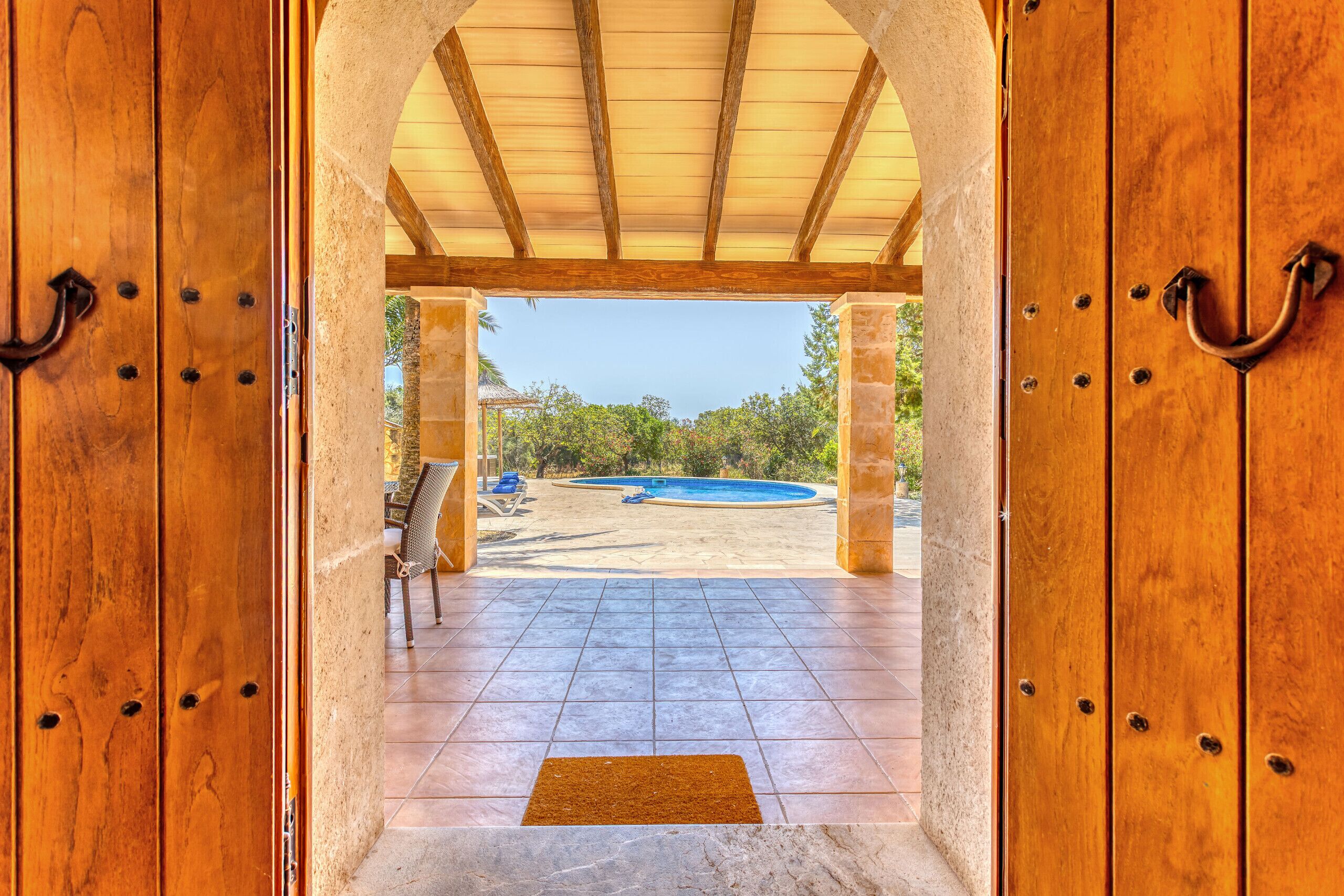 Eine Holztür führt zu einer überdachten Terrasse mit Pool, Sitzgelegenheiten im Freien und Blick auf die umliegende Landschaft.