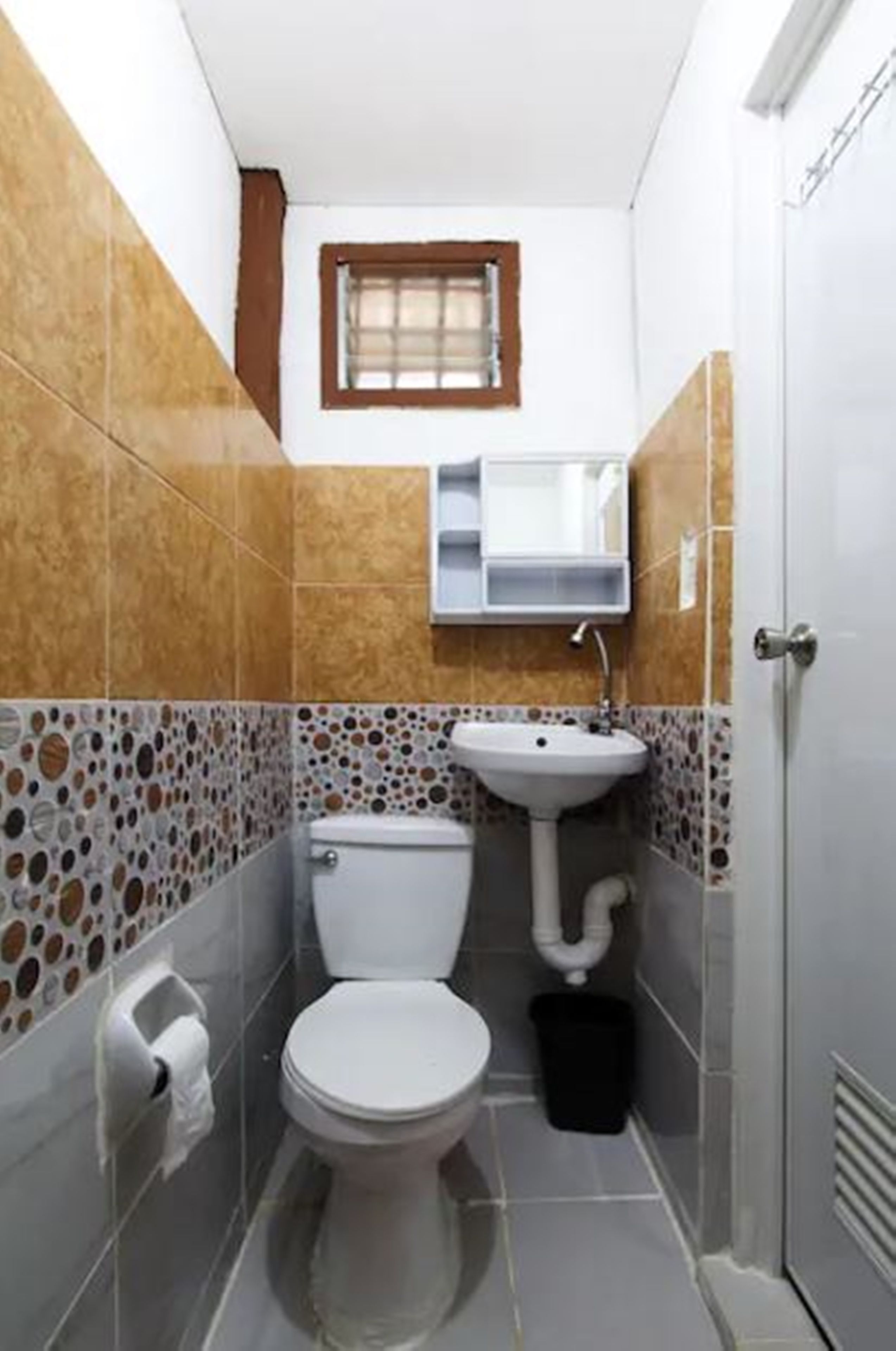 Une petite salle de bain avec des toilettes, un lavabo et une fenêtre située au-dessus du miroir.