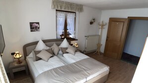 Une chambre à coucher avec un grand lit, une table de chevet avec une lampe, une fenêtre avec des rideaux, un porte-manteau et une porte.