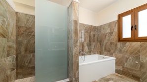 Un baño moderno con cabina de ducha de vidrio, una bañera independiente y paredes con azulejos de mármol.