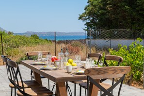 An outdoor dining table with chairs, set with plates, glasses, and a fruit bowl.
