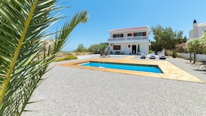 Una casa de dos pisos con piscina, mobiliario exterior y jardín.