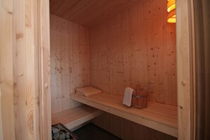 A wooden sauna with benches, a towel rack, and a stone heater.
