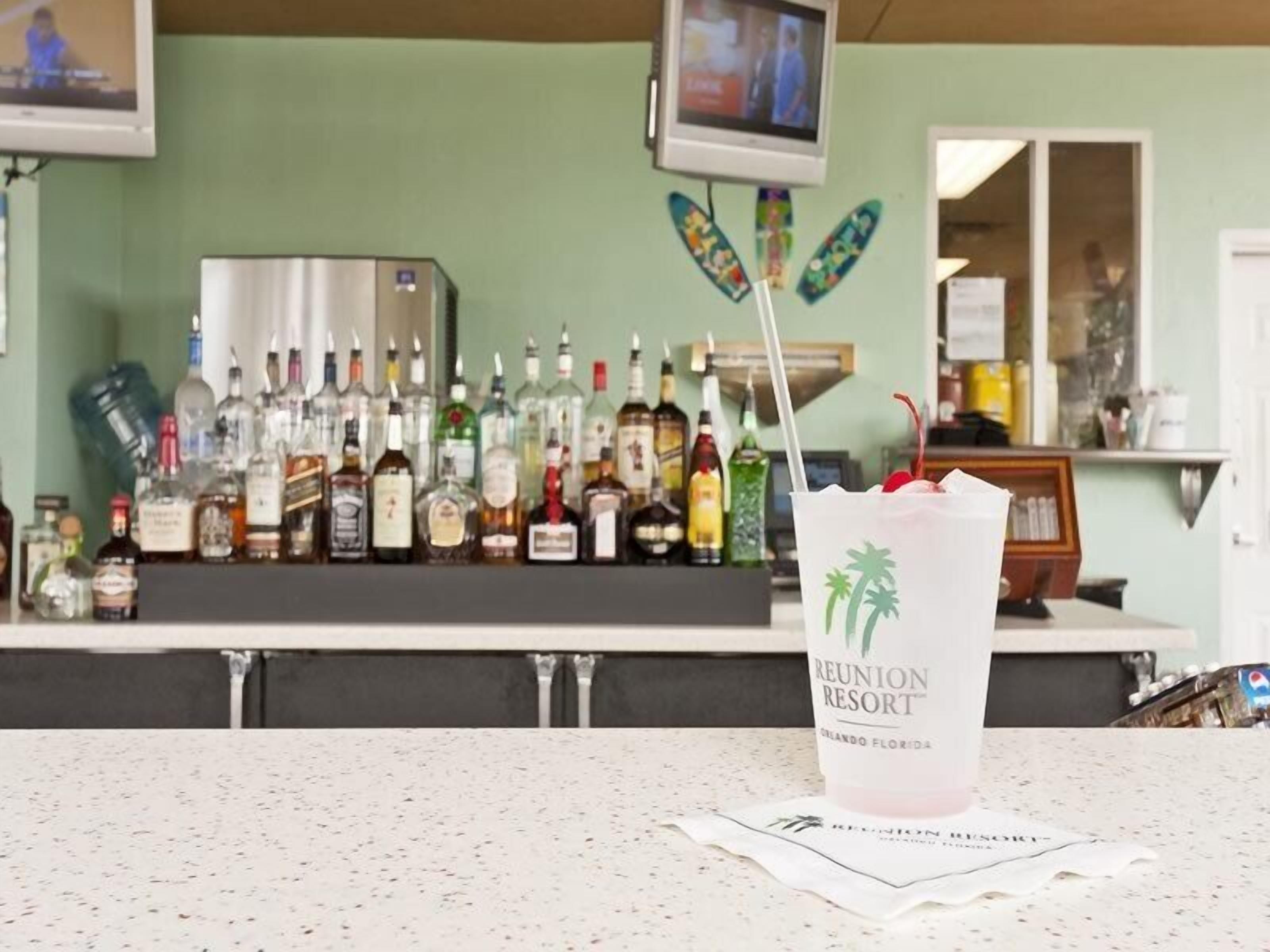 A bar area with a variety of liquor bottles, a television screen, and a drink with a straw on the counter.