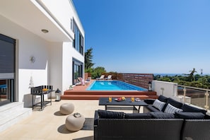 Eine moderne Außenterrasse mit Pool, Sitzgelegenheit und Meerblick.