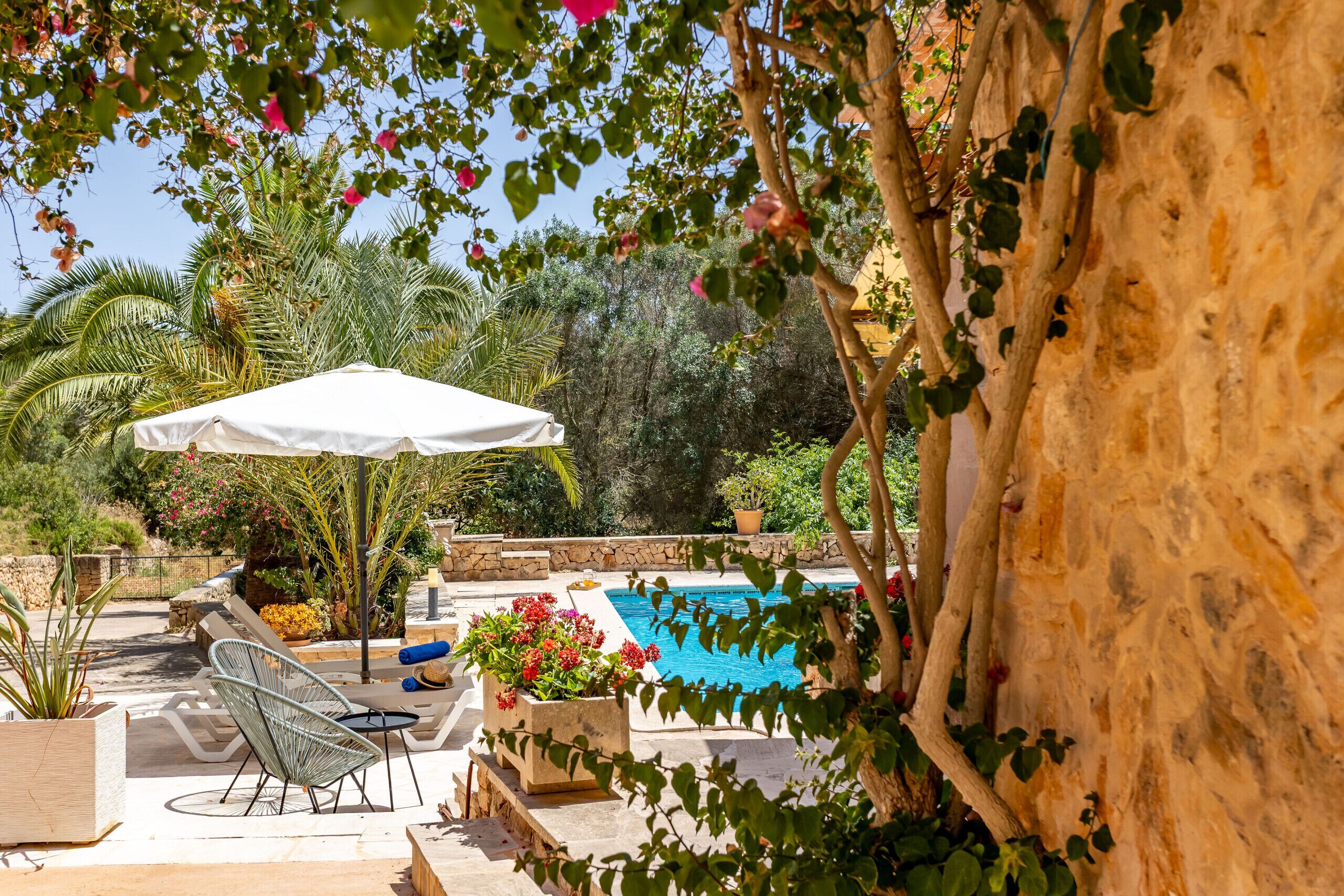 A poolside area with a white umbrella, lounge chairs, and a stone wall.