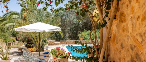 A poolside area with a white umbrella, lounge chairs, and a stone wall.