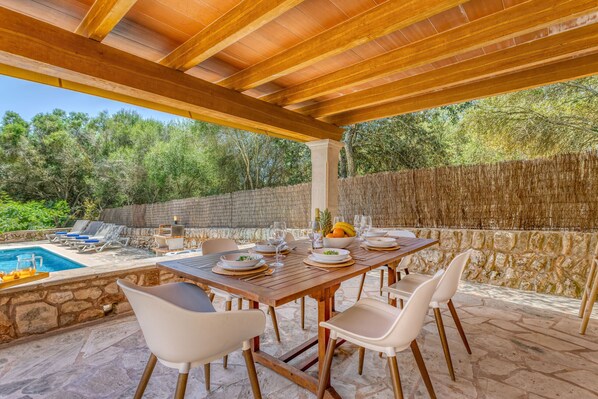 An outdoor dining area with a pool, stone walls, and a wooden pergola.
