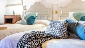 Un lit bien fait, agrémenté de coussins à motifs et d’une couverture, une table de chevet en bois avec une lampe, et une tête de lit blanche.