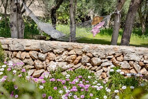 Una hamaca atada entre árboles, un muro de piedra y un jardín lleno de flores.