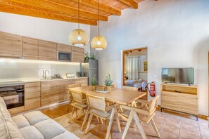 A modern kitchen with wooden cabinets, a dining area with a wooden table and chairs, and a living area with a sofa and a television.