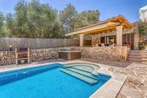 A swimming pool with a stone wall and a pergola with outdoor seating.