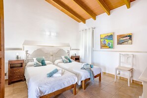 Een slaapkamer met twee bedden, houten hoofdborden, nachtkastjes, een stoel en twee schilderijen aan de muur.