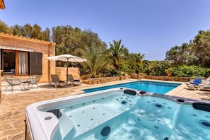 A swimming pool with a hot tub, outdoor seating, and a stone wall.