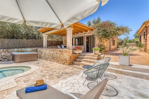 Área da piscina com hidromassagem, assentos ao ar livre e um pérgola para criar sombra.