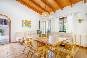 A dining area with a wooden table and chairs, a white sofa, and a large window with curtains.