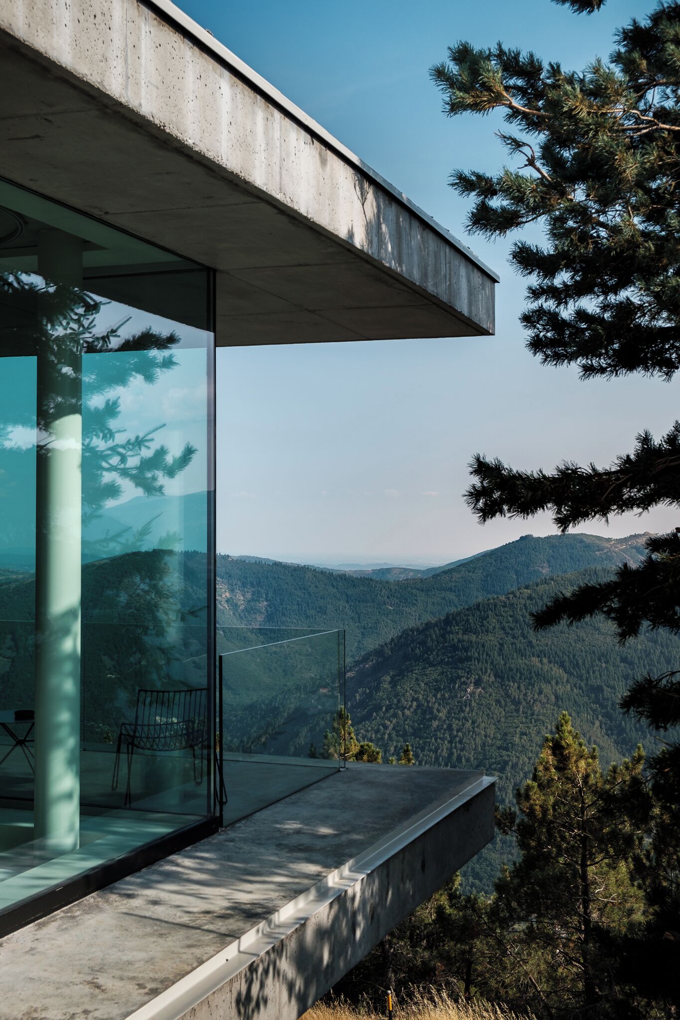 Un edificio moderno con fachada de vidrio, un alero de hormigón y vistas a un paisaje montañoso.