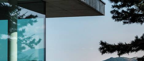 Un edificio moderno con fachada de vidrio, un alero de hormigón y vistas a un paisaje montañoso.