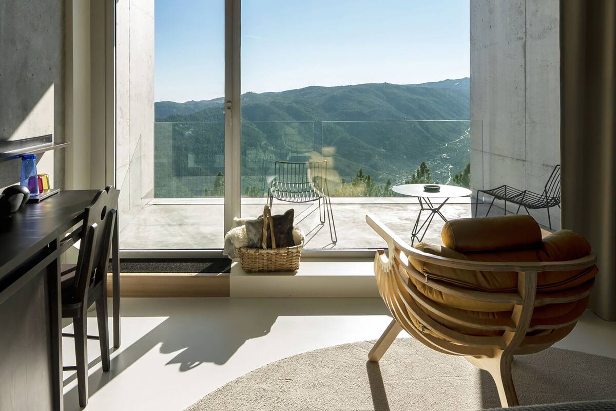A modern room with a large window offering a mountain view, a dining area with a table and chairs, and a cozy seating area with a cushioned chair.