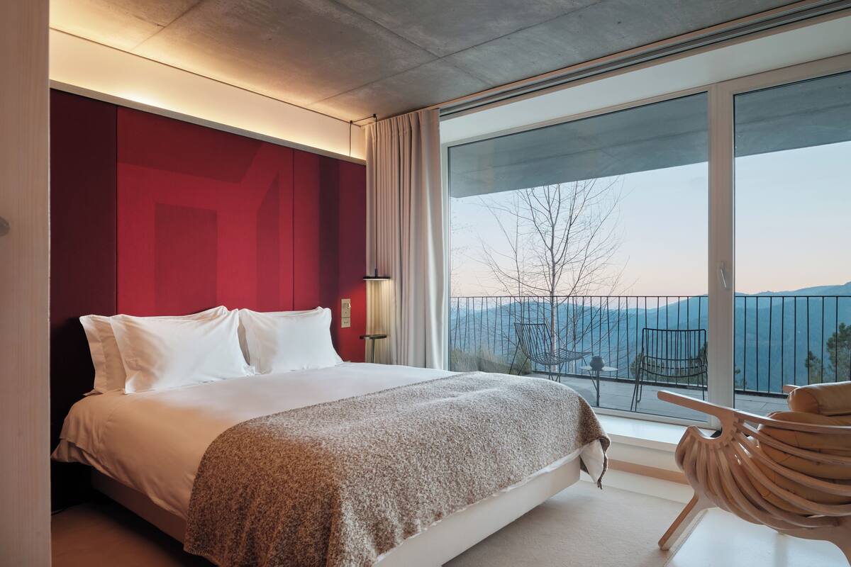 A modern hotel room with a large bed, a view of the mountains, and a balcony with a chair.