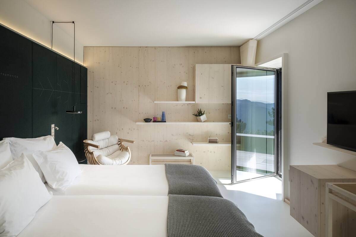 A modern bedroom with a large bed, a chair, a desk, and a TV.