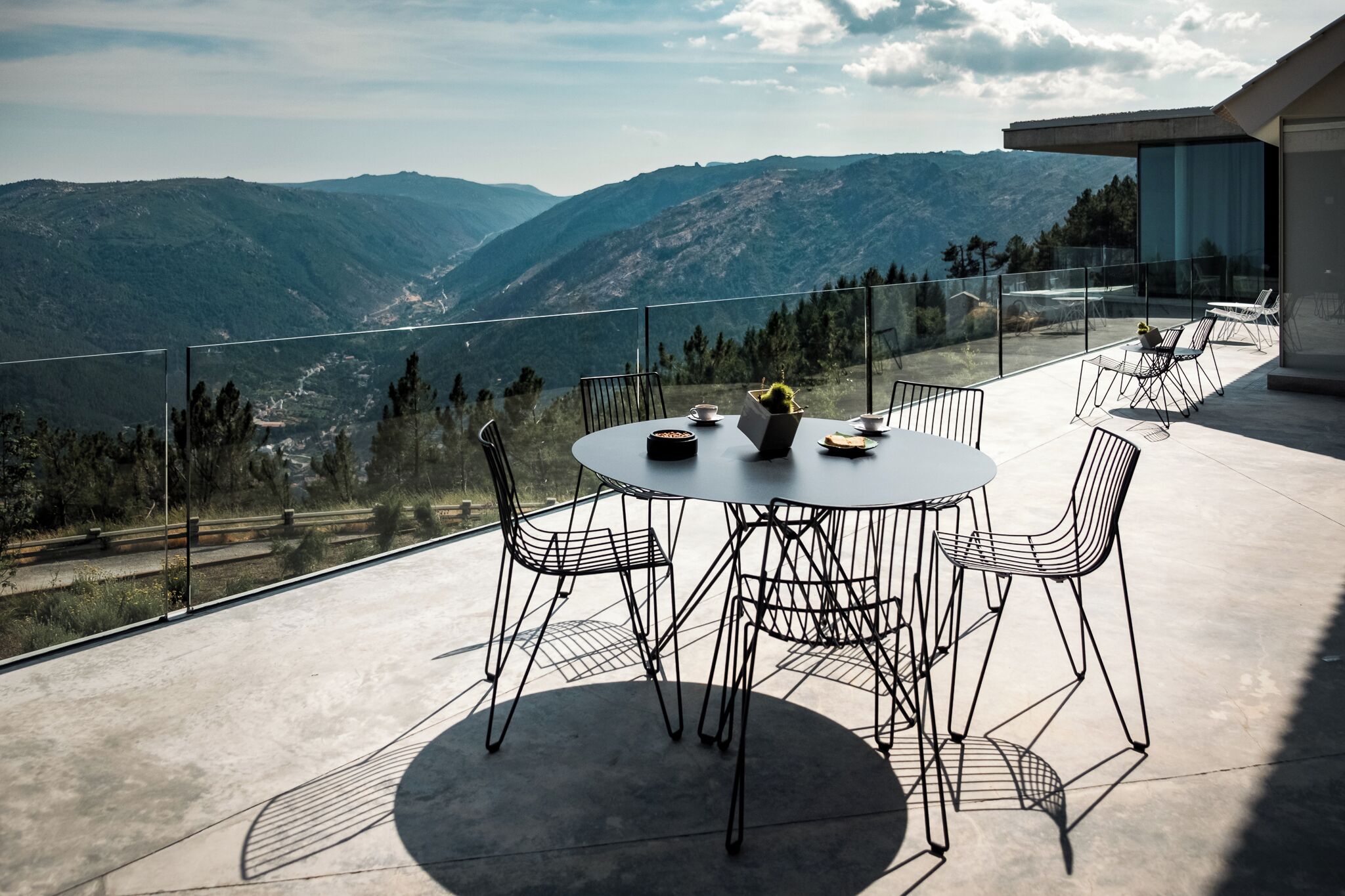 Een ronde tafel met stoelen op een balkon met uitzicht op een bergachtig landschap.