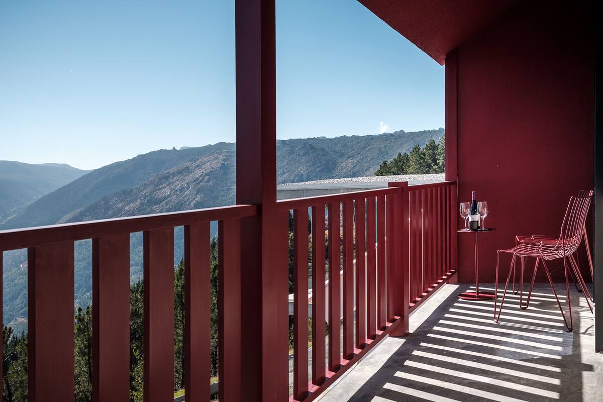A balcony with a red railing, a table with a wine glass, and a chair.