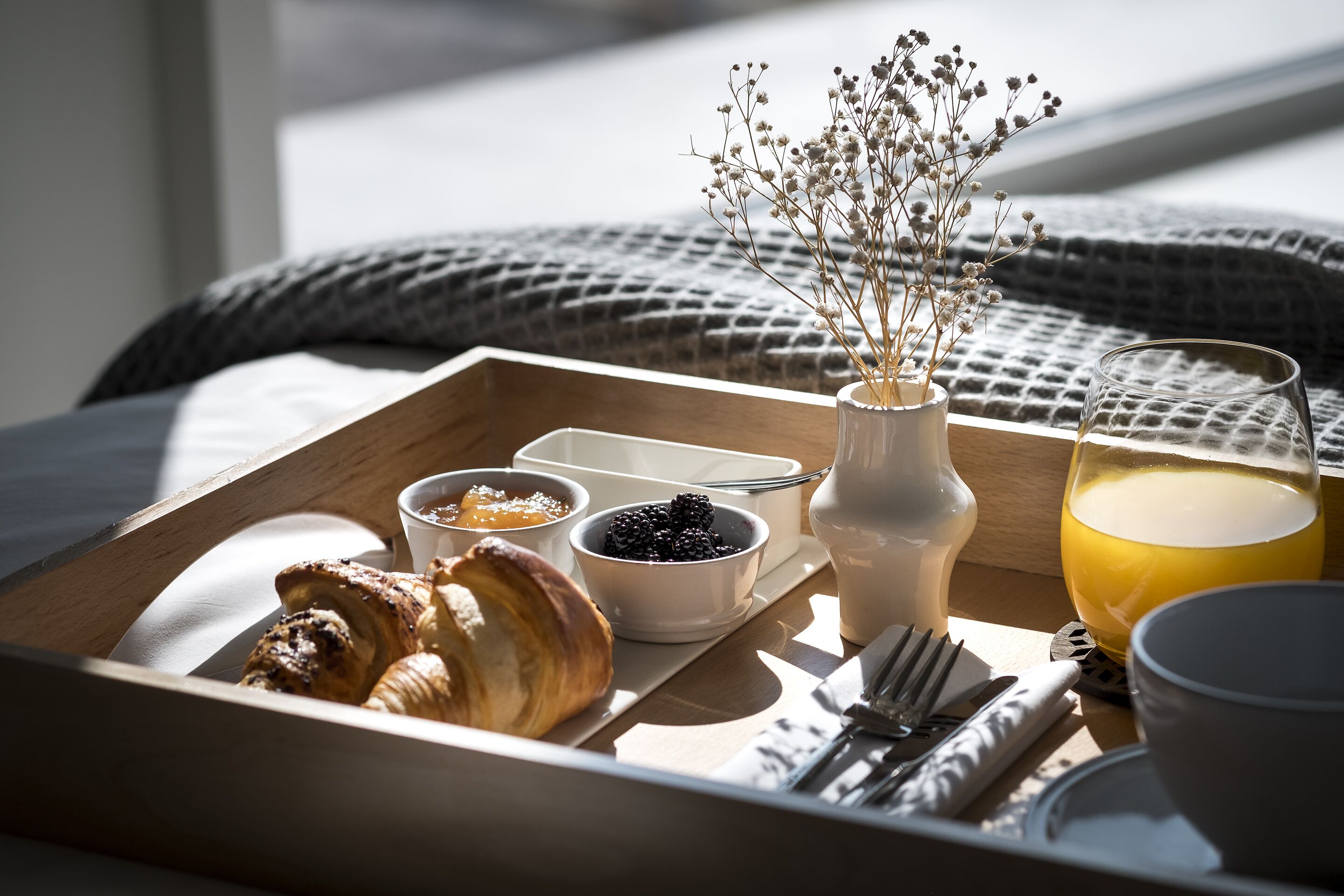 Aamiaistarjotin, jossa on croissantteja, marjoja ja lasi appelsiinimehua puupöydällä.
