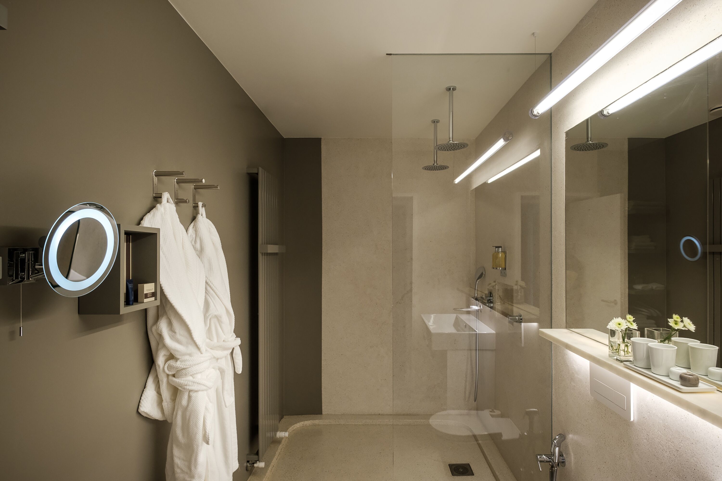 A modern bathroom with a glass-enclosed shower, a vanity with a mirror, and a robe hanging on a rack.