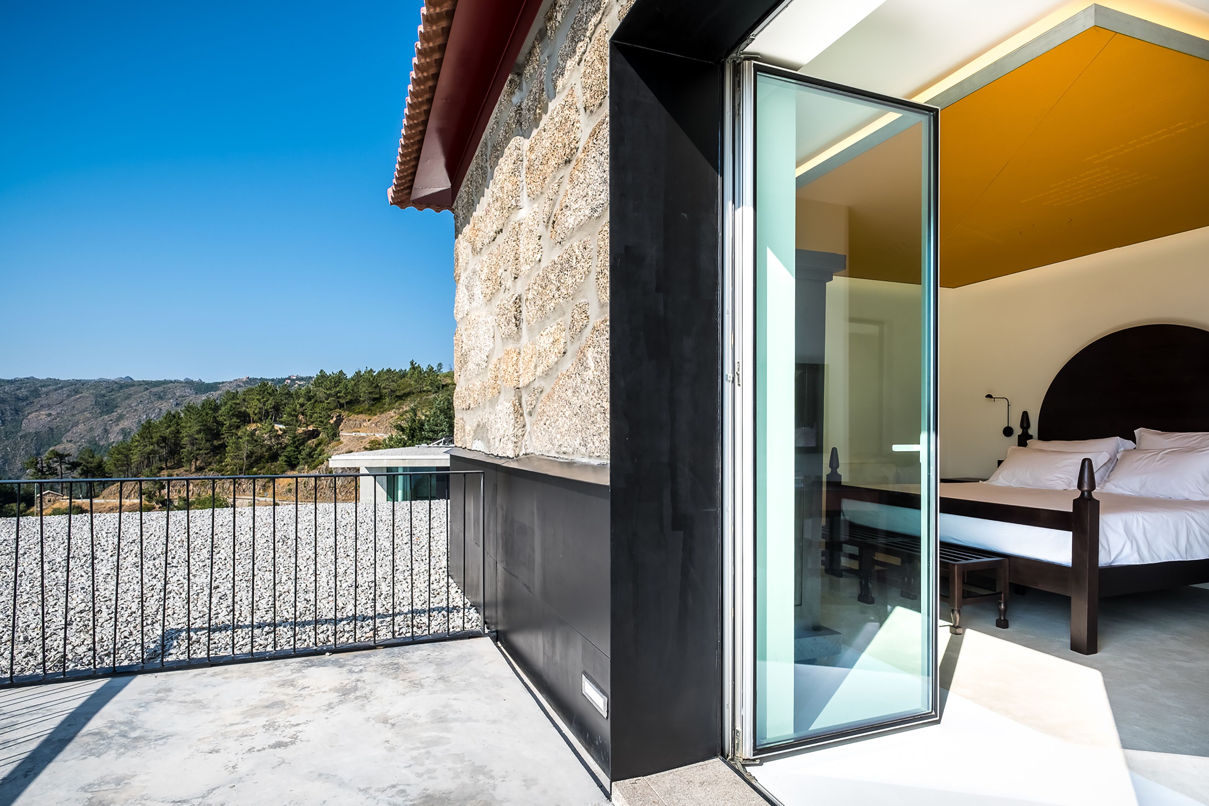 A modern bedroom with a glass door, a bed, and a view of the mountains.