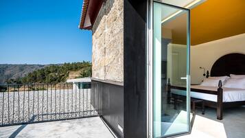 A modern bedroom with a glass door, a bed, and a view of the mountains.