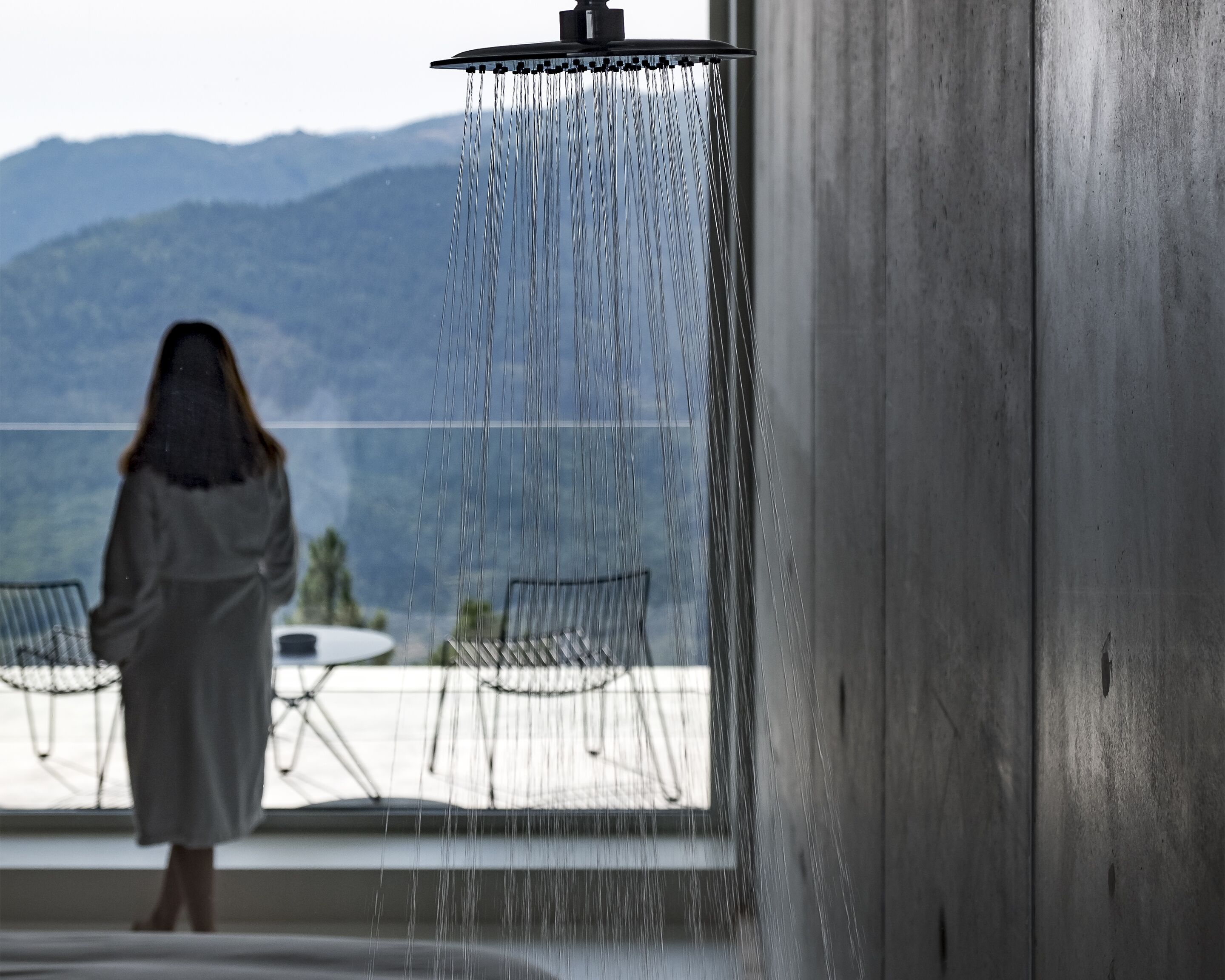A person standing under a shower with a view of mountains in the background.