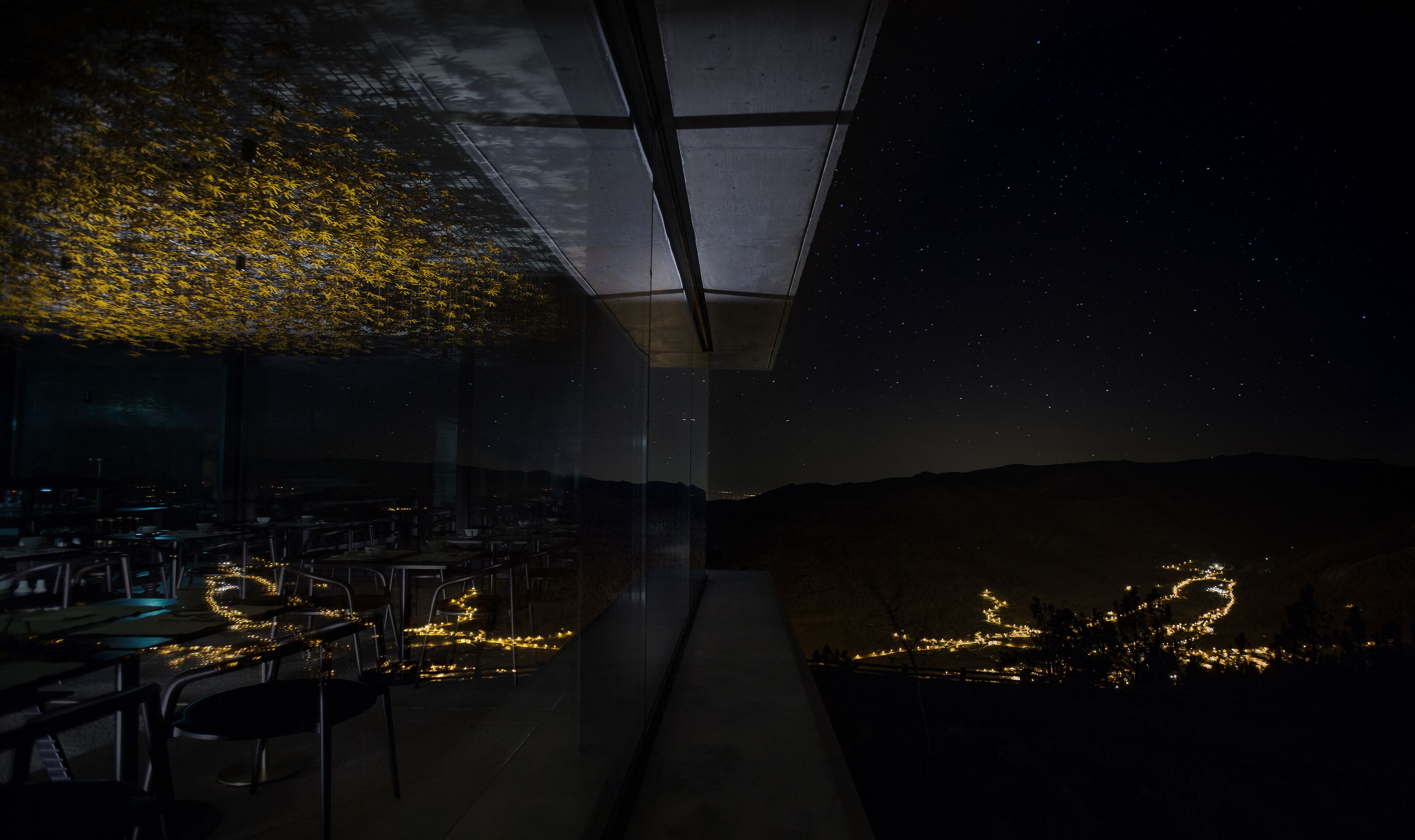 A restaurant with outdoor seating, a glass ceiling, and a view of the night sky.