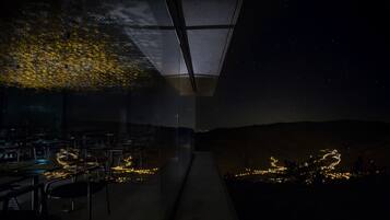 A restaurant with outdoor seating, a glass ceiling, and a view of the night sky.