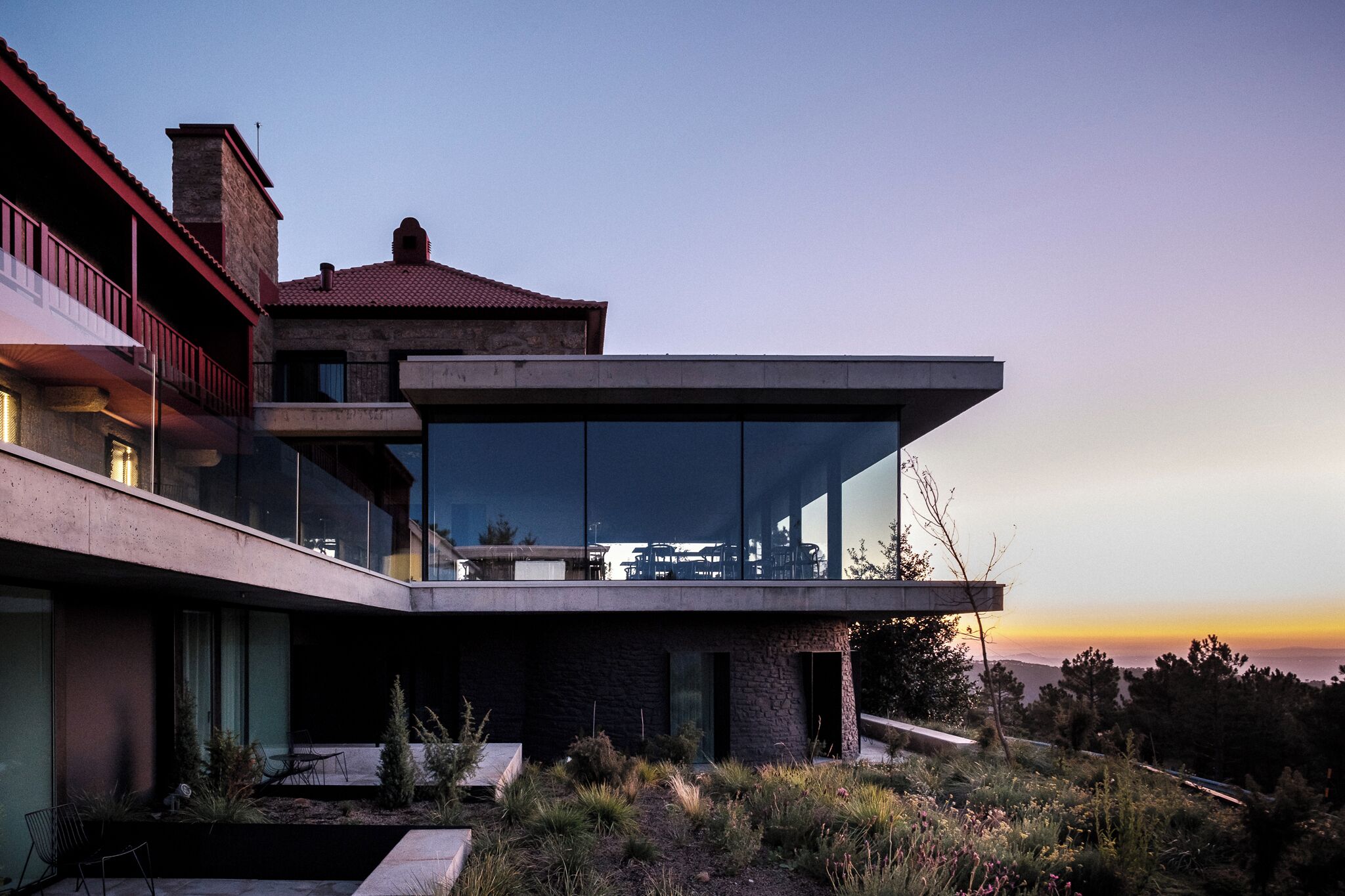 Uma casa moderna com fachada de vidro, varanda e vista para o pôr do sol.