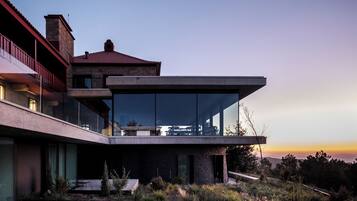 Uma casa moderna com fachada de vidro, varanda e vista para o pôr do sol.