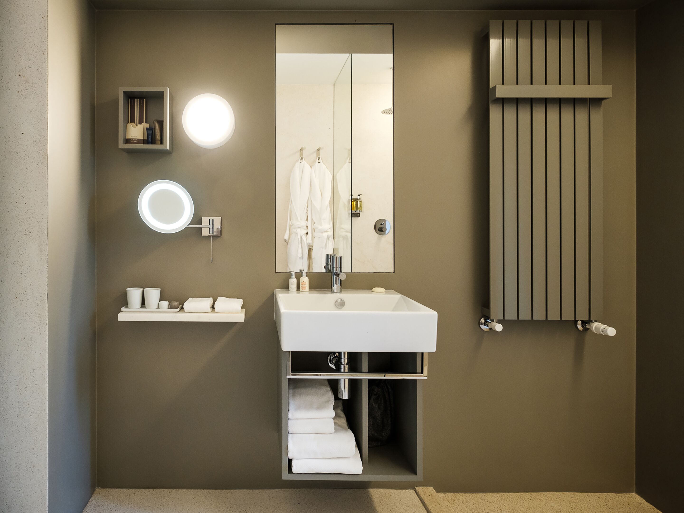A modern bathroom with a large mirror, a round light, a towel rack, and a built-in heater.
