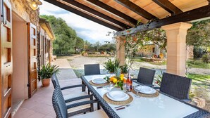 Un espacio de comedor al aire libre con una mesa dispuesta para cuatro personas, rodeada de sillas de mimbre, bajo una pérgola de madera.