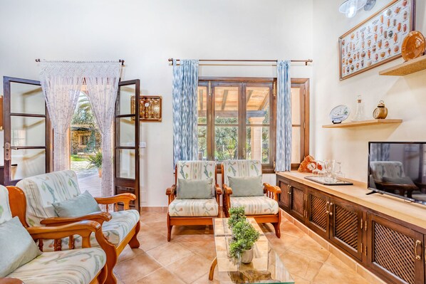 Una sala de estar con dos sillones de madera, una mesa de centro de vidrio y un televisor sobre un mueble de madera.