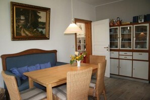 A dining area with a wooden table, wicker chairs, a blue sofa, and a painting on the wall.