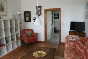 A living room with a red armchair, a patterned sofa, a television, and a bookshelf.