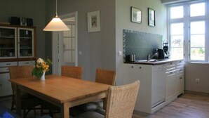 A kitchen with a wooden dining table, wicker chairs, a hanging light fixture, and a window with a view.