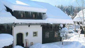 Une maison recouverte de neige, avec une façade sombre, une porte bien visible et des glaçons qui pendent du toit.