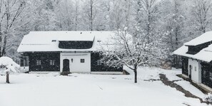 Una casa cubierta de nieve con puerta principal, un pequeño porche y un árbol al frente.