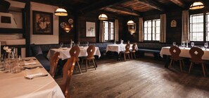 A restaurant with wooden floors, tables set with white tablecloths, and wooden chairs. - Apartment Schwindelfrei - Naturel Hoteldorf SCHÖNLEITN (Latschach am Faaker See)